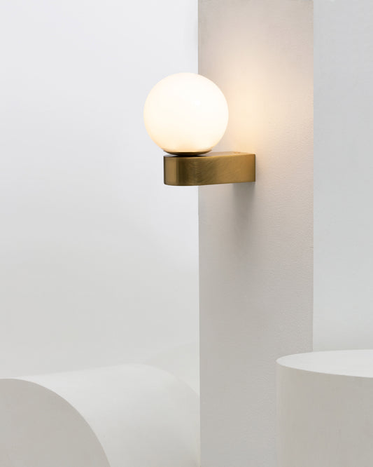 Modern wall sconce with a round hand-blown glass shade mounted on a neutral wall, creating a soft ambient glow ideal for contemporary interiors in melbourne, australia 