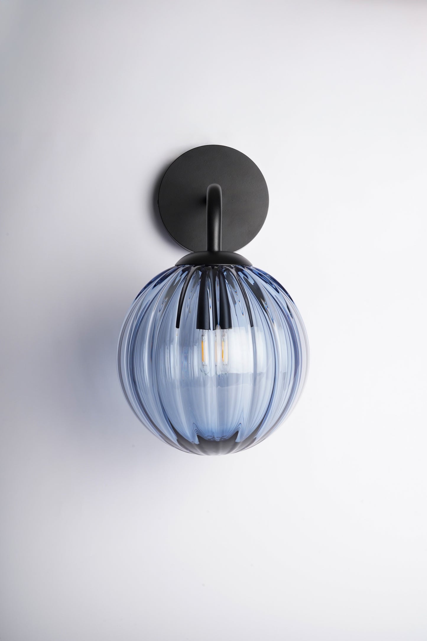 Wall-mounted light fixture with blue glass shade on a white background