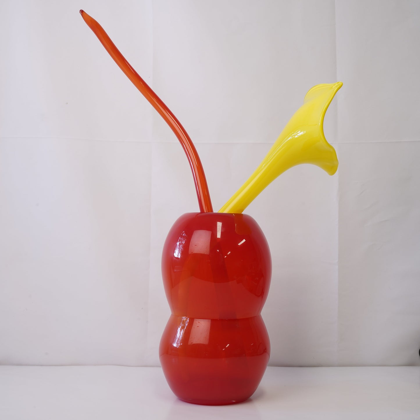 Red hand-blown glass vase with sculptural handblown glass flowers and yellow prongs, creating a bold, artistic statement piece for interiors
