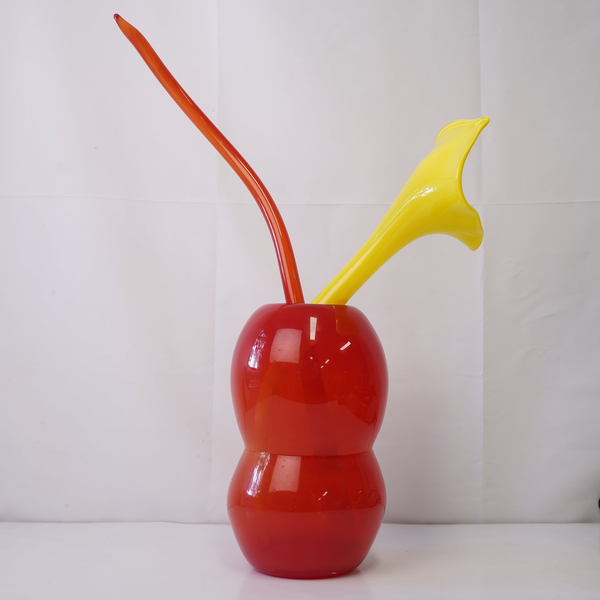 Red hand-blown glass vase with sculptural handblown glass flowers and yellow prongs, creating a bold, artistic statement piece for interiors
