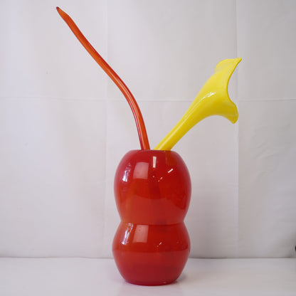 Red hand-blown glass vase with sculptural handblown glass flowers and yellow prongs, creating a bold, artistic statement piece for interiors
